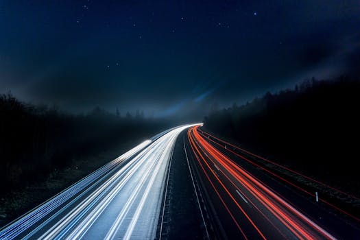 Long exposure night shot capturing stunning red and white light trails on a highway under a starry sky.